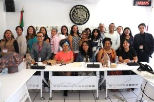 personas sentadas y de pie en un salón blanco con el escudo nacional