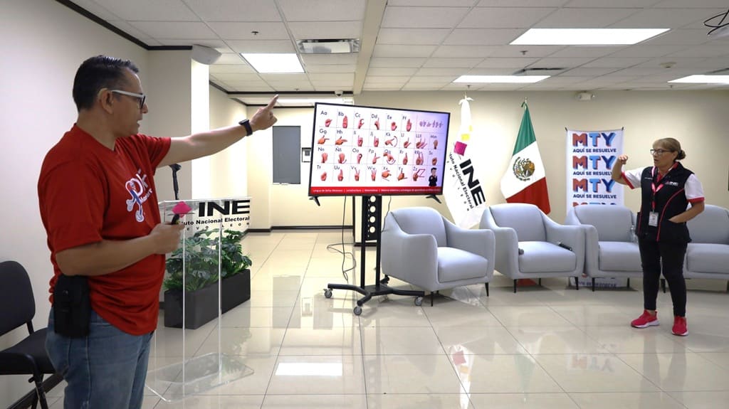 Un hombre señalando a una mujer, en medio un pizarrón