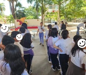 una mujer de pie frente hablando con un micrófono a estudiantes