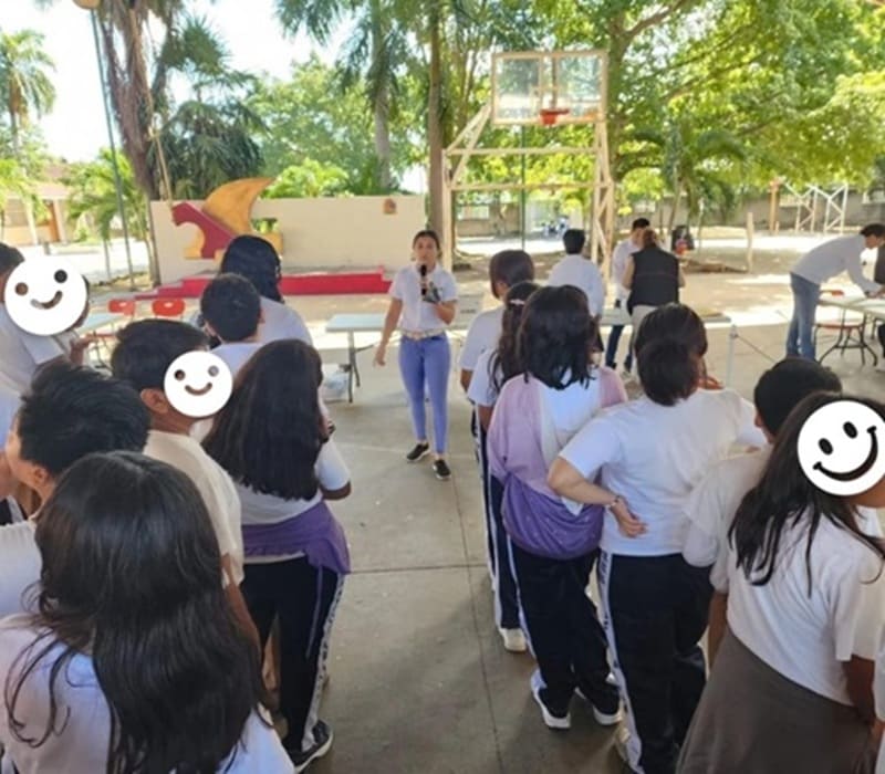 una mujer de pie frente hablando con un micrófono a estudiantes