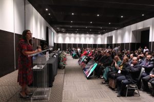 Persona participantes sentadas en el salón enfrente del público asistente en el evento.