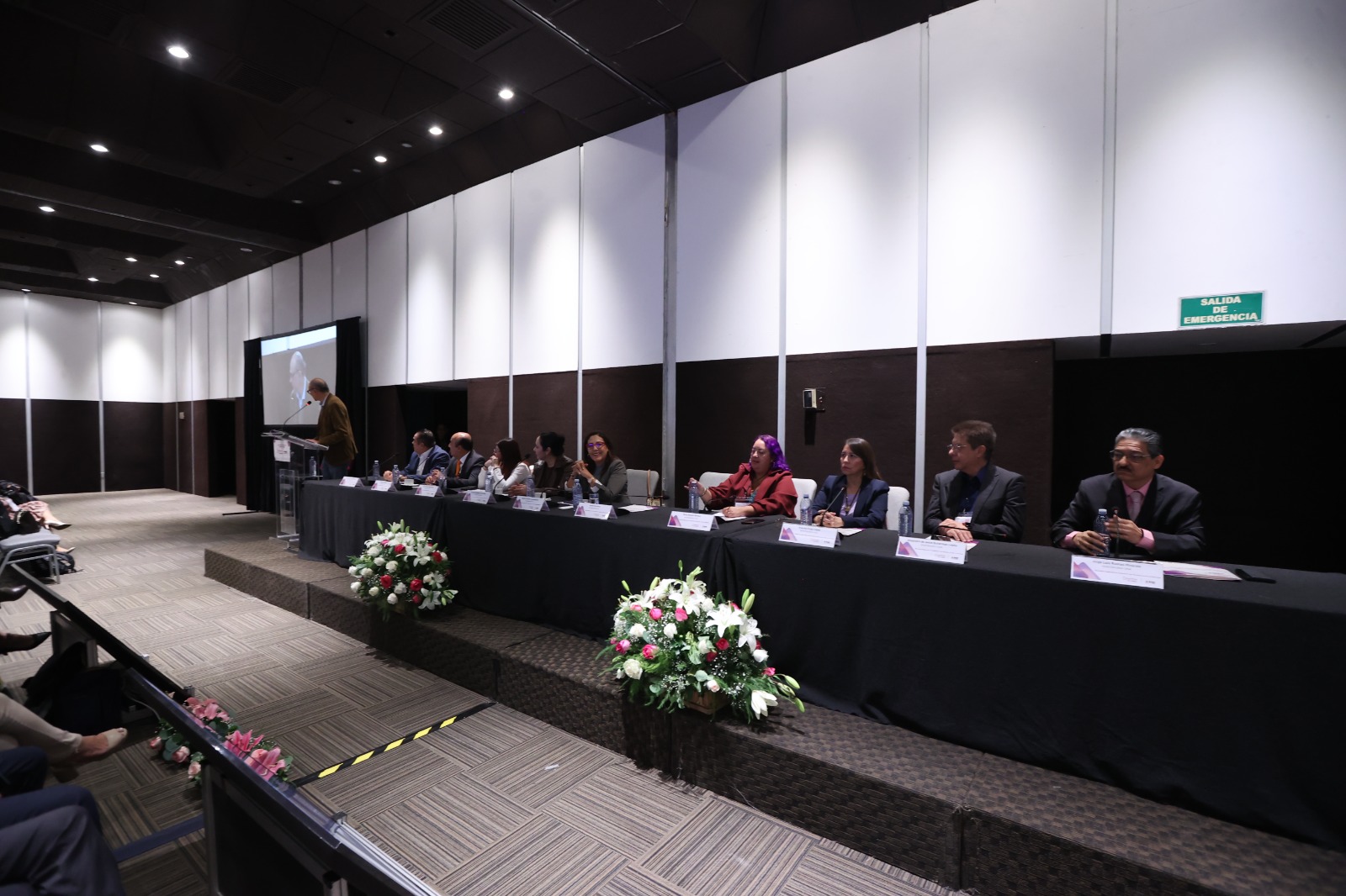 Persona participantes sentadas en el estrado frente al público asistente durante su participación en el evento.