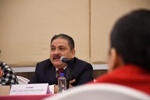 hombre con bigote sentado y hablando frente a un micrófono