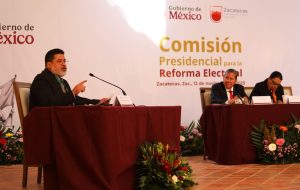 tres personas sentadas frente a mesas con micrófonos