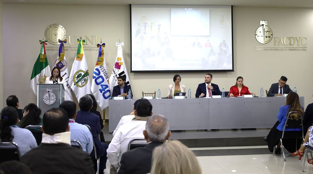 un salón con varias personas sentadas escuchando a una mujer hablando