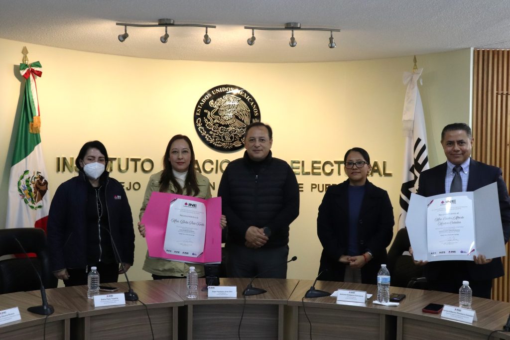 cinco personas de pie, una mujer y un hombre sostienen reconocimientos