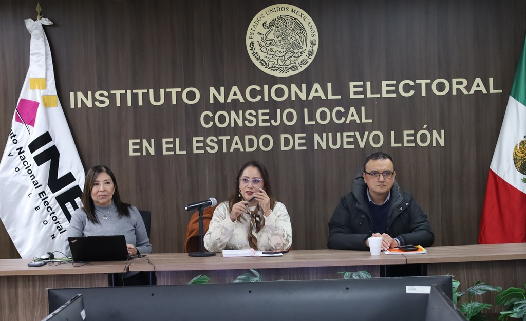 Dos mujeres y un hombre sentados frente a dos banderas