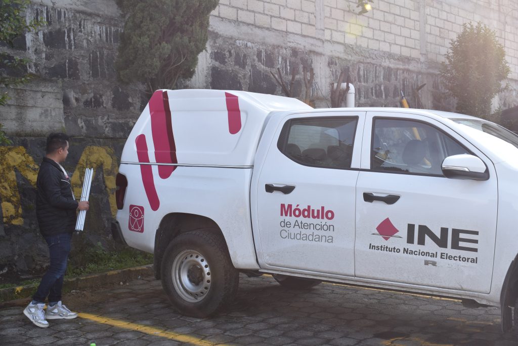 Una camioneta blanca con líneas rosas y letras negras con la leyenda INE