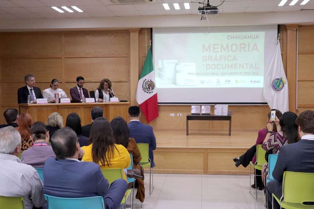 Cuatro personas sentadas detrás de una mesa. Delante de ellas, quince personas sentadas prestando atención