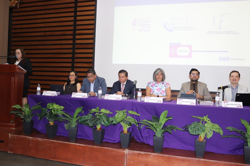 Seis personas sentadas en una mesa larga hablando detrás de un micrófono