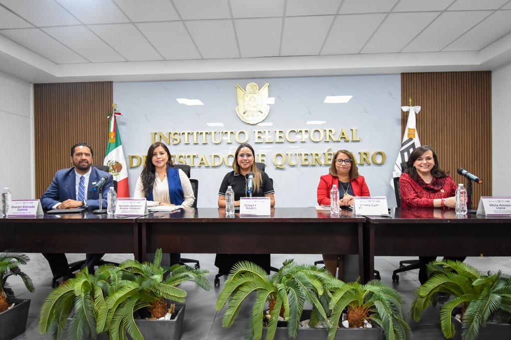 Cinco personas sentadas detrás de una mesa larga hablando detrás de micrófonos