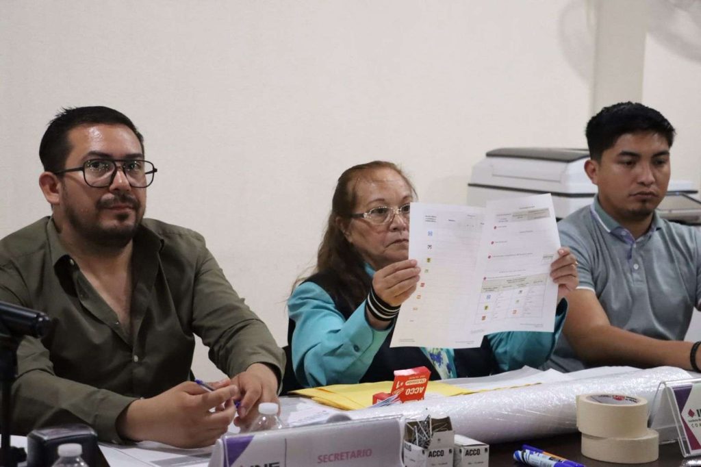 Personas sentadas mostrando boletas electorales.