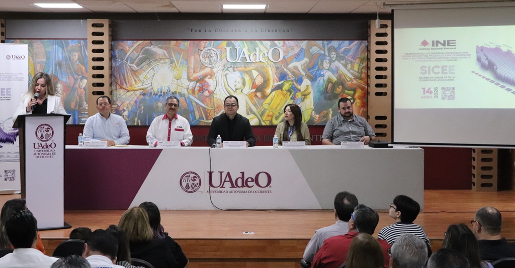 cinco personas sentadas y una de pie hablando frente a un micrófono