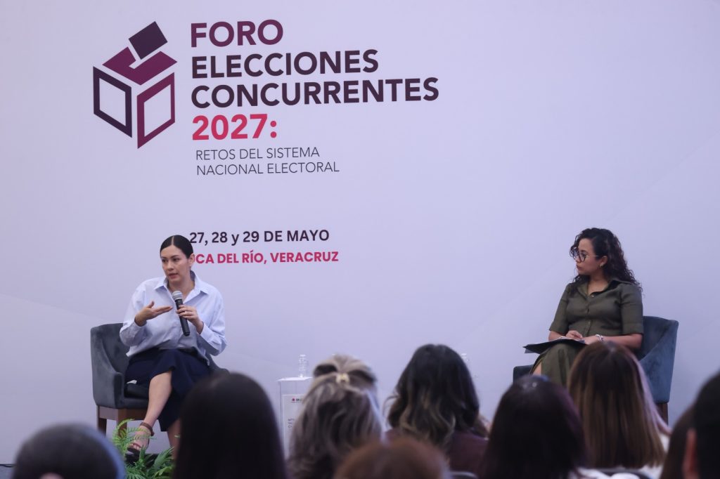 Personas participantes sentadas en el estrado frente al público asistente.