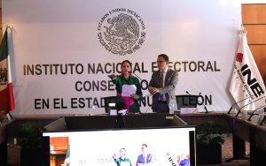 mujer de pie con el brazo derecho extendido al frente, mientras un hombre sostiene un micrófono
