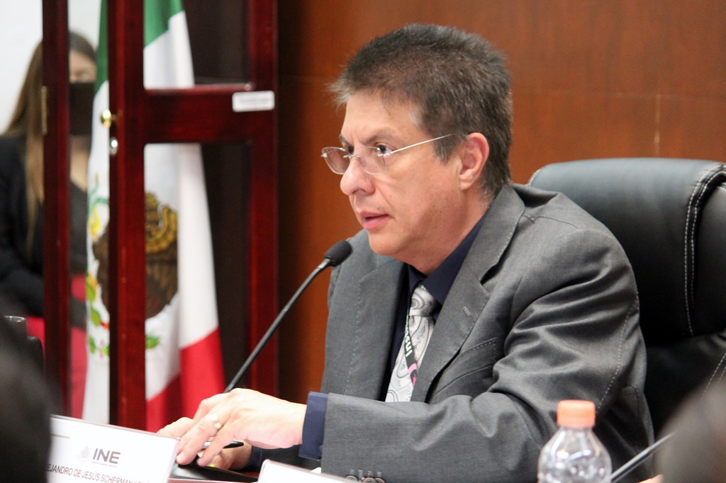 hombre de lentes y traje gris, sentado frente a un micrófono la toma es lateral