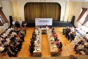 personas en un teatro sentadas algunas frente a una mesa y otras en sillas a los extremos del lugar