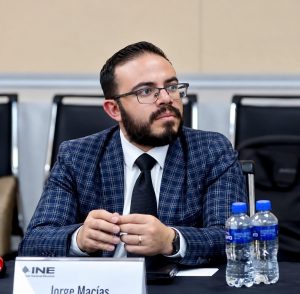 hombre de barba y lentes sentado con traje azul a cuadros