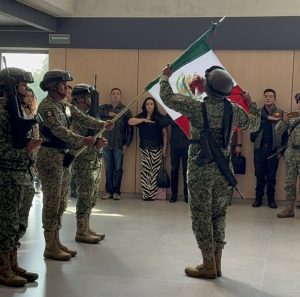 tres militares en fila horizontal sosteniendo la bandera nacional