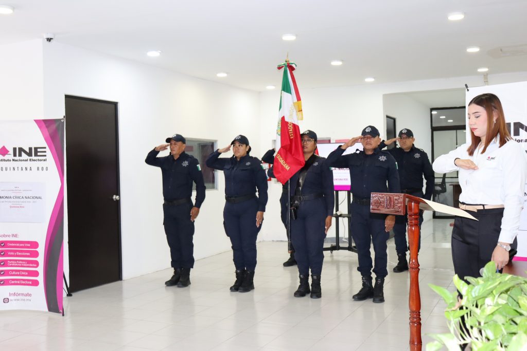 cinco personas uniformadas de pie en línea horizontal sosteniendo la bandera nacional