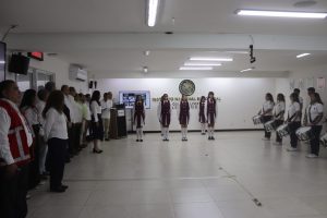 cinco estudiantes uniformadas de pie en línea horizontal sosteniendo la bandera nacional