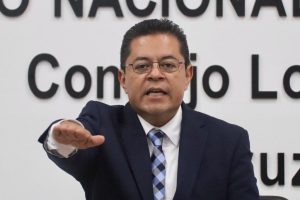 un hombre de lentes y traje negro con el brazo derecho extendido al frente