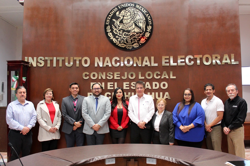 diez personas de pie frente a una pared de madera con escudo nacional y letras doradas