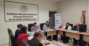 siete personas en un salón blanco sentadas al rededor de una mesa