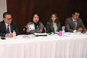 cuatro personas sentadas , una de ellas muestra una credencial para Votar
